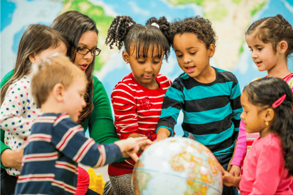Group of preschool children and teacher looking at a globe in the classroom.