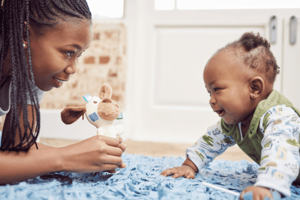 Woman holds a toy out to a baby who is doing tummy time