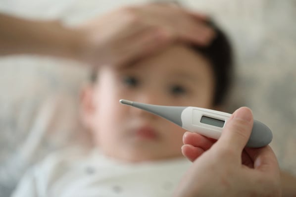 Adult laying hand on young boy's head measuring for a fever and looking at a thermometer