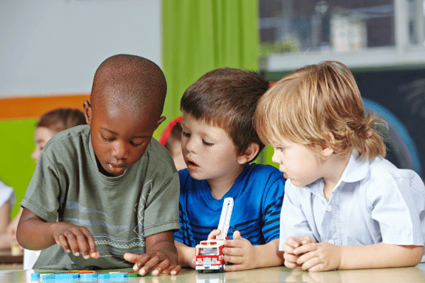 Preschool children playing with building blocks at a desk.