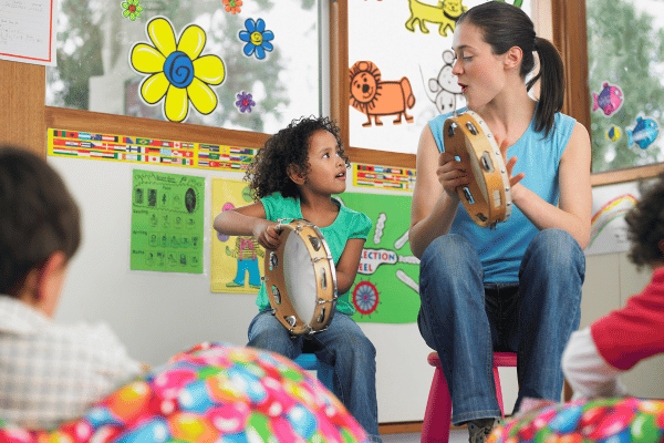 Preschool teacher in music class shaking a tambourine with young girl