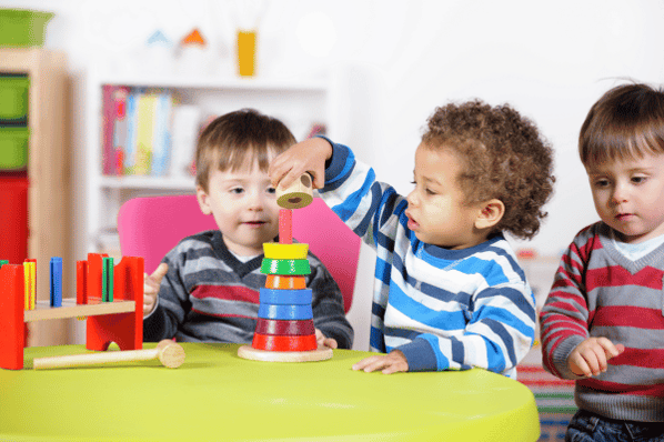 Group of toddlers playing with multi-colored wooden toys.