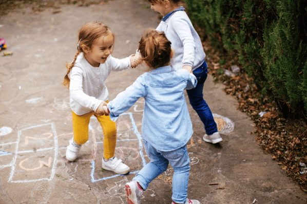 Group of three toddler girls playing hopscotch outside