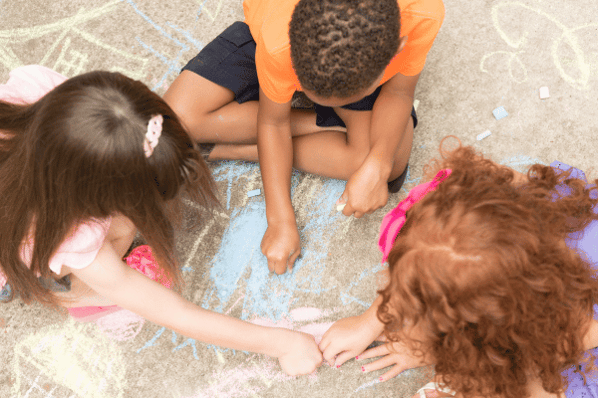 Group of children drawing with sidewalk chalk outside on the pavement.