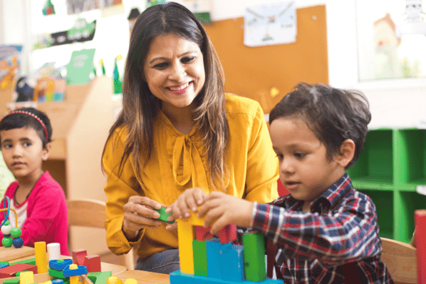 Teacher playing with building blocks with child.