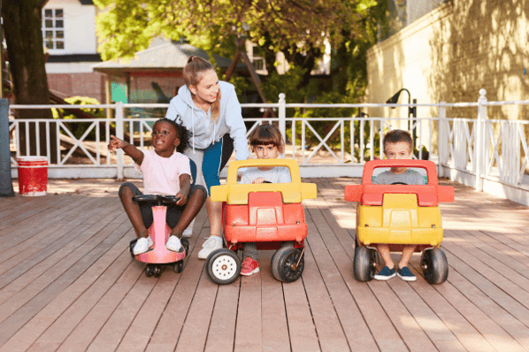 Children at daycare drive in pedal cars.