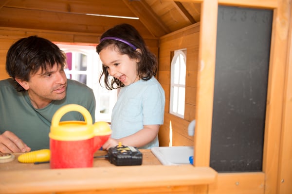 man crouching next to young girl in a small wooden house play structure