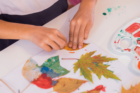 A child's hands doing an arts and crafts project with leaves and paint.