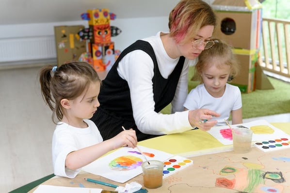 woman showing two young girls how to use paints