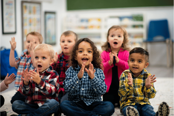 multi-ethnic group of preschool children clapping and singing along to a song