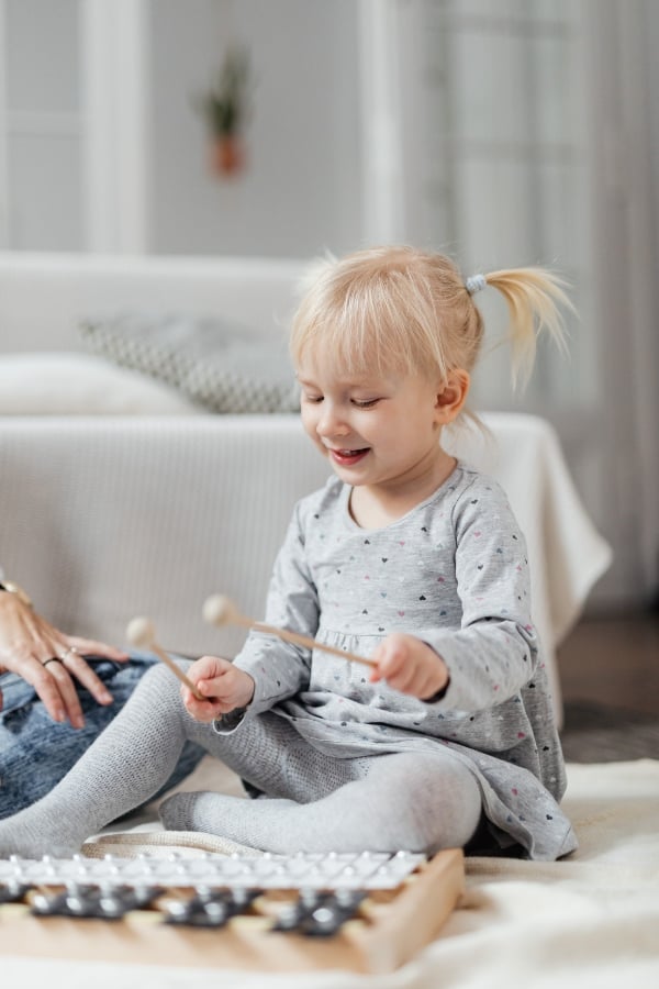 A little girl sitting on the floor and holding a pair of mallets above a xylophone.