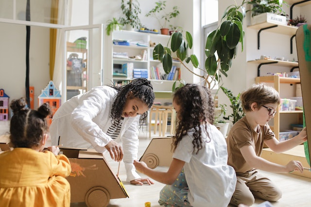 Teacher painting a cardboard box with children