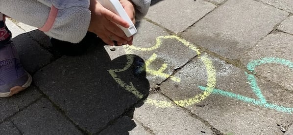 child draws the letter F on the sidewalk with yellow chalk