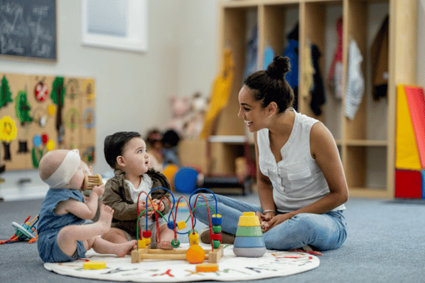 Two toddlers sitting on the floor with teacher at a childcare center.
