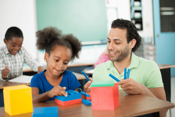 male teacher helping young girl build structure with colorful legos
