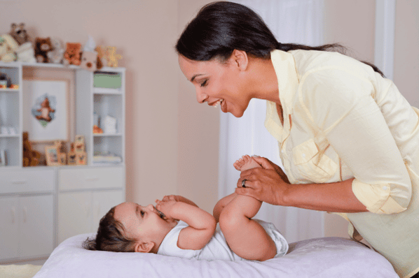 Woman looking at baby lying on their back on a changing table. They are both smiling at each other.