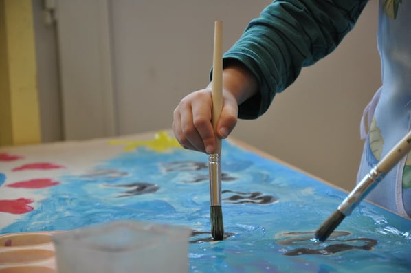child using paintbrush to paint with light blue paint