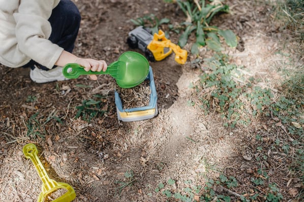 child kneels outside in the dirt and scoops dirt into a toy truck