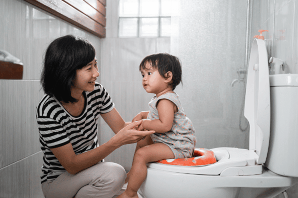 Woman helping child sit on a toilet with a child friendly seat.