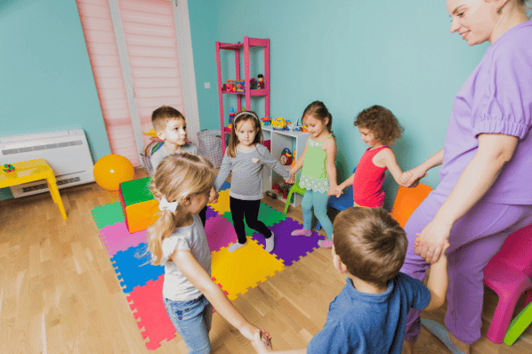 Teacher and children holding hands and walking in a circle in a preschool classroom.