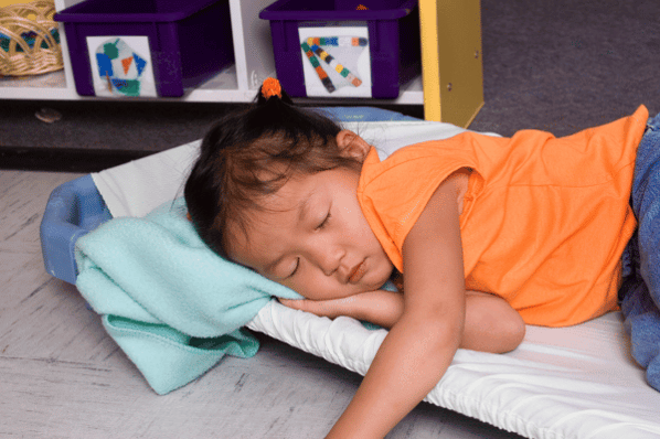 Child asleep on cot at daycare.