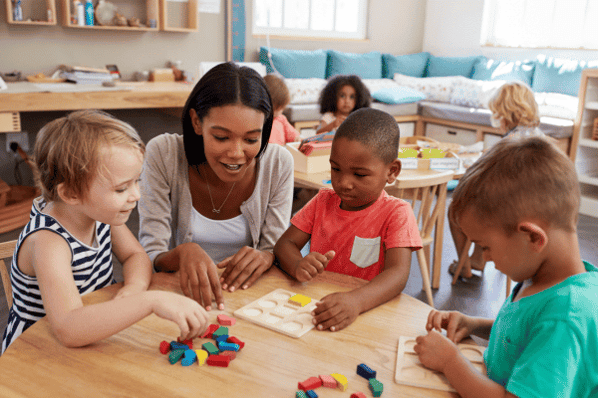 Teacher in Montessori classroom doing puzzles with children sitting at a desk.