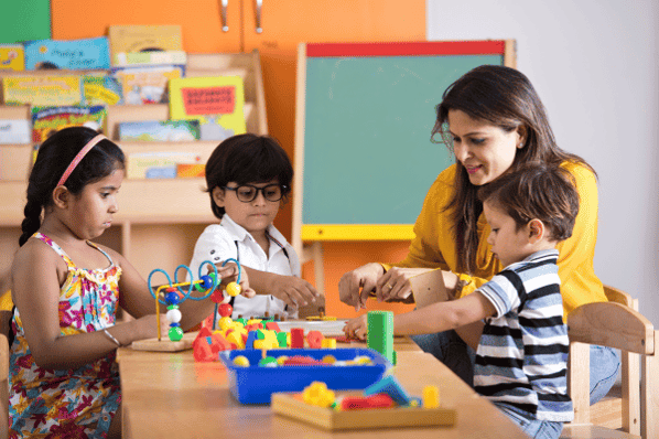 Teacher sitting at table with 3 preschool aged children as they play with blocks