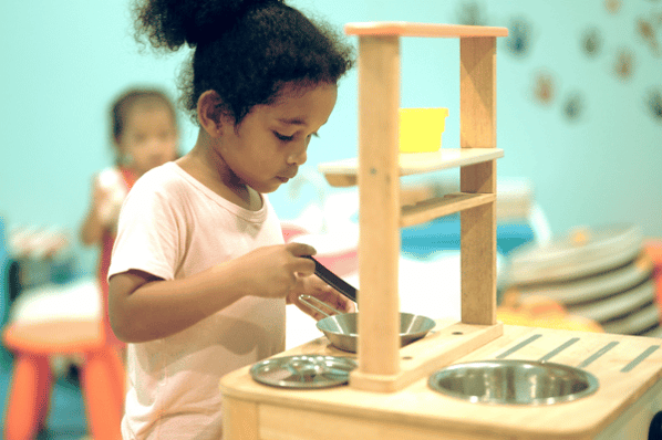 Little girl pretends to cook in preschool classroom