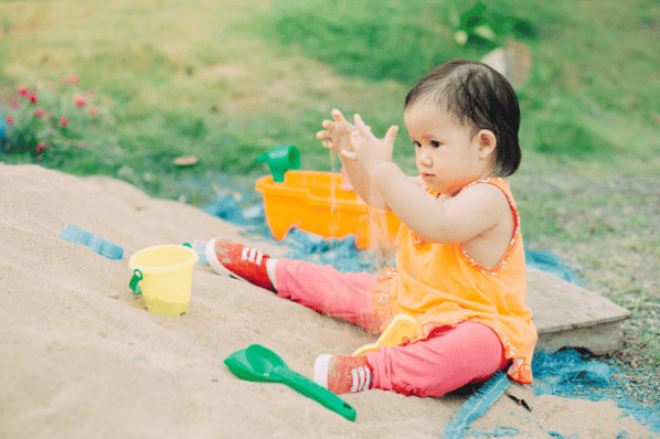 Young child playing alone in a sandbox outside.