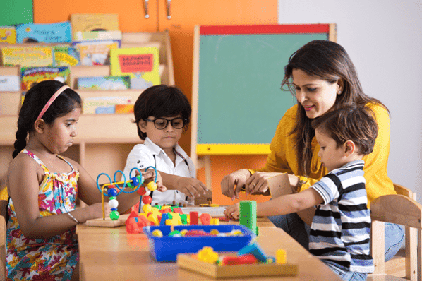 Teacher sitting with three children at a table observing them play with puzzles.