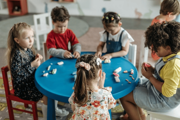 children sitting at a round table playing with clay
