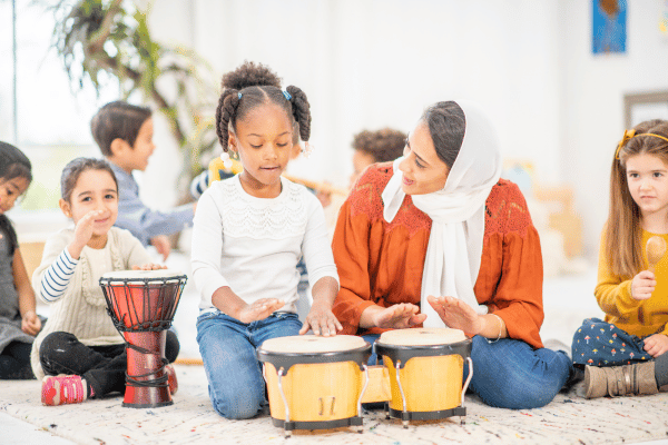 A teacher plays a set of bongo drums with young child during preschool music class.