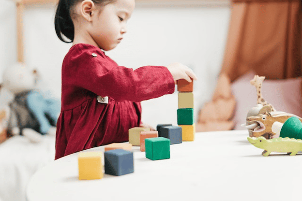 Young girl in a red dress stacking blocks on a desk