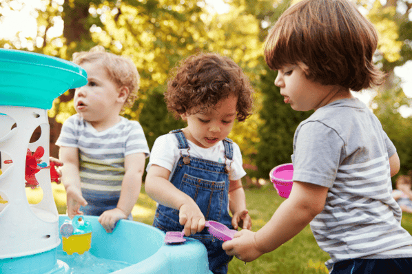 Preschool children playing at a water table outside.