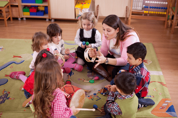 Preschool children and teacher sitting in a circle playing with musical instruments.