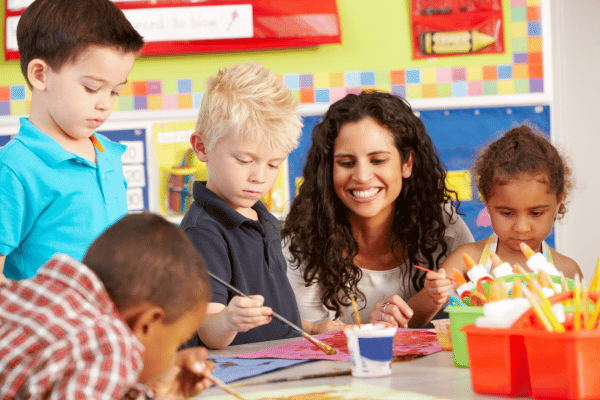 teacher watches as four preschool children paint with watercolors on construction paper