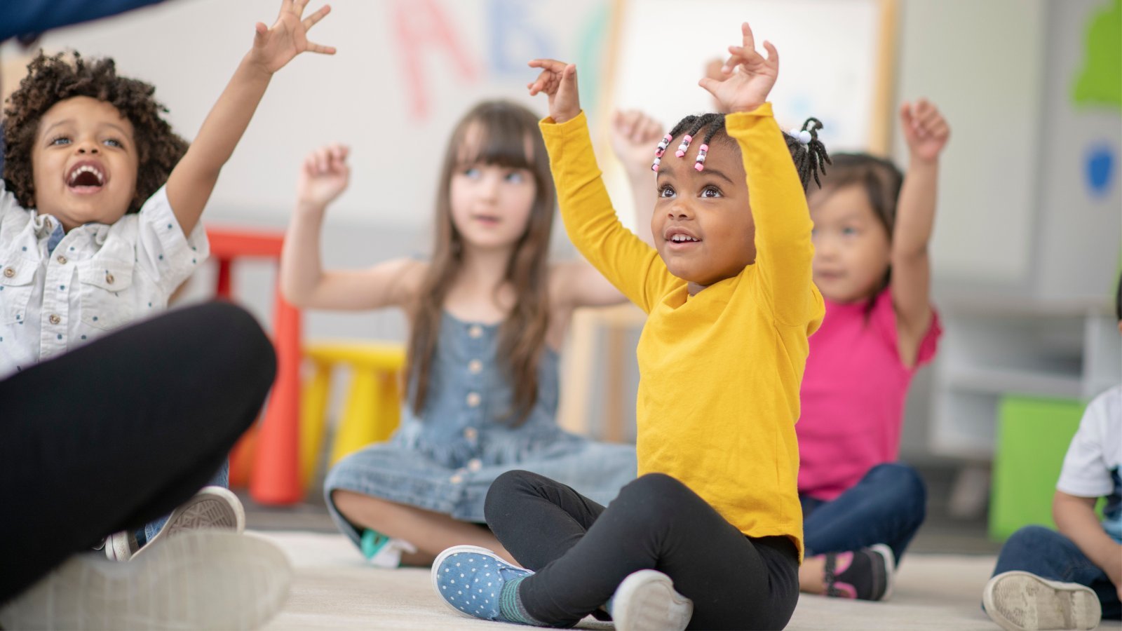 Kids Sitting On Carpet With Teacher And Learning To Pronounce