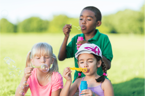 three young children blow bubbles outside
