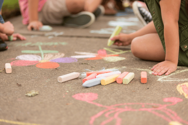 a group of children drawing flowers on pavement with colorful sidewalk chalk